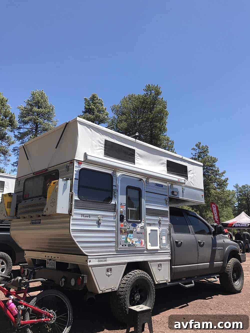 A red Toyota Tundra pickup truck with a large, elevated camper shell, featuring aggressive off-road tires and suspension.