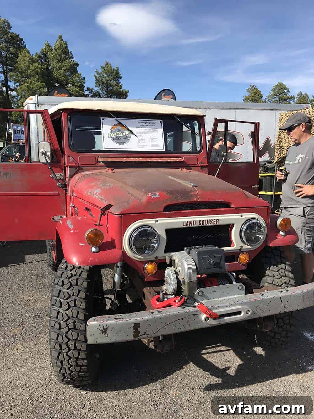 A red Toyota Tacoma with an integrated camper, parked at a scenic outdoor location, showcasing its readiness for adventure.