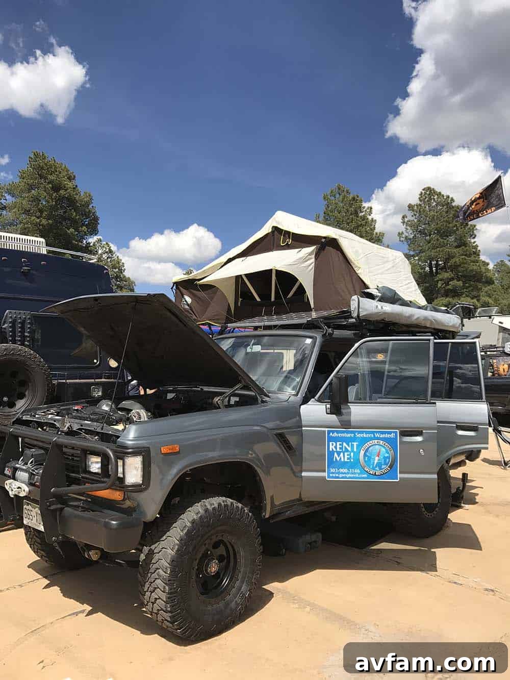 A white Ford F-Series pickup truck with an elaborate expedition camper, featuring exterior storage and an awning.
