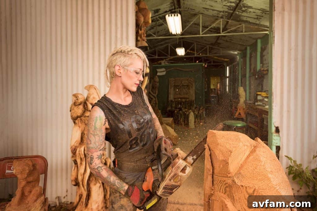 Griffon Ramsey, world-renowned chainsaw carver, poses with a detailed wood sculpture. Her artwork showcases intricate designs achieved with powerful tools, merging ruggedness with refined artistry.