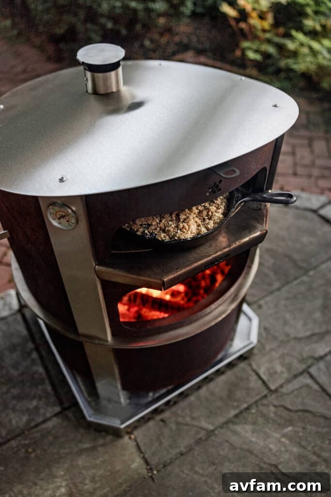 A person slides a fresh pizza into the Breeo Live-Fire Pizza Oven with a wooden peel.