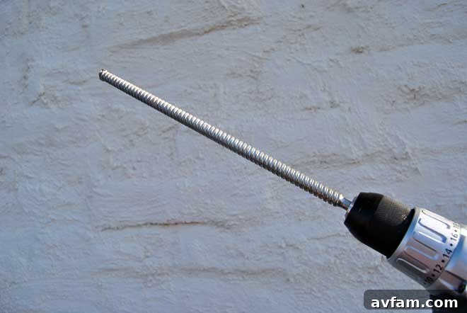 Cordless Drill with Masonry Bit Close-up of a powerful cordless drill fitted with a long, carbide-tipped masonry drill bit, ready for tough drilling tasks in dense soil