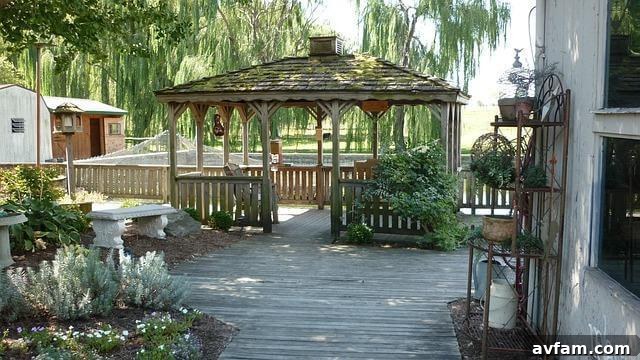 A wooden walkway leading to a tranquil backyard gazebo surrounded by greenery.